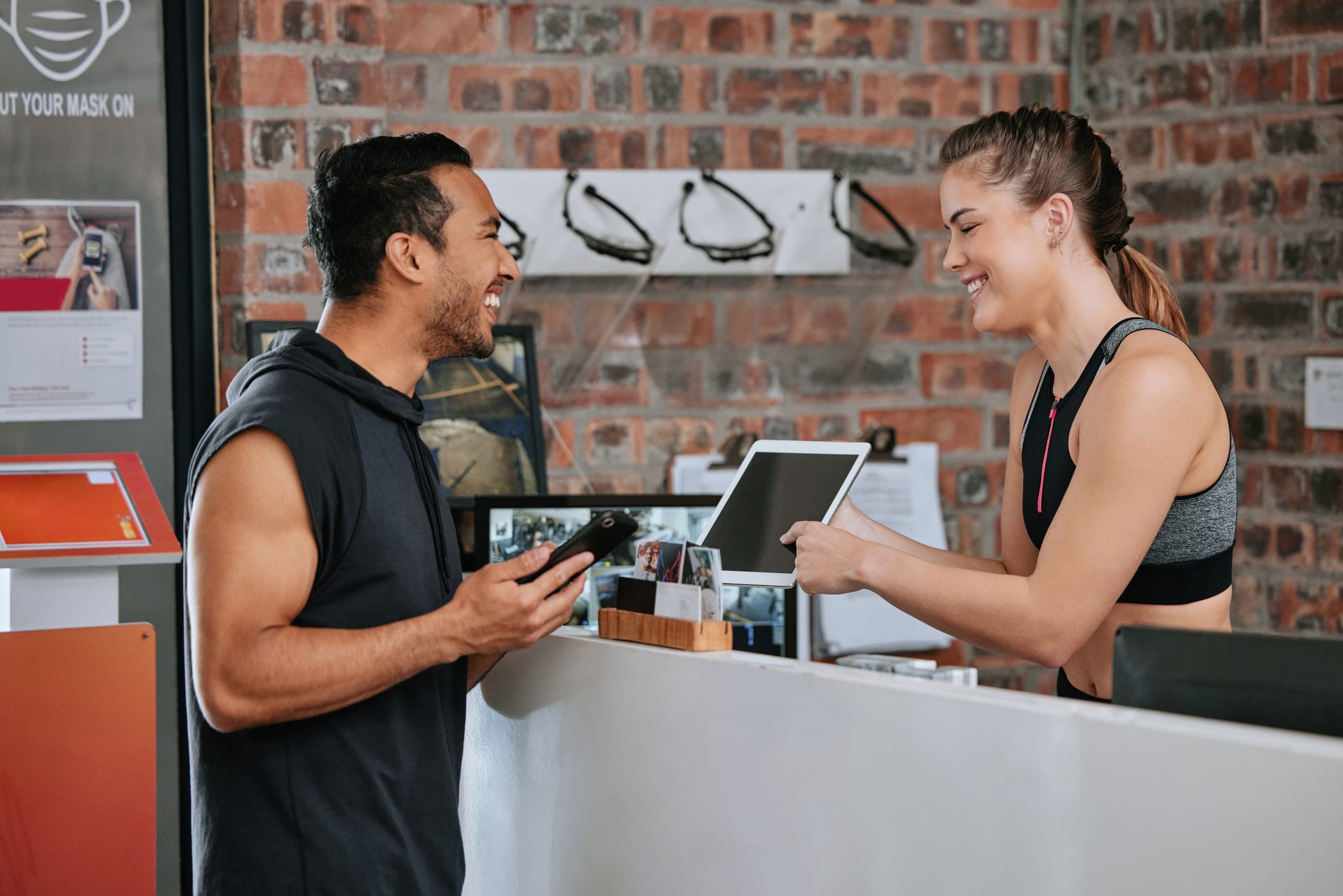 Gym staff processing a credit card payment on a tablet at the front desk of a fitness facility