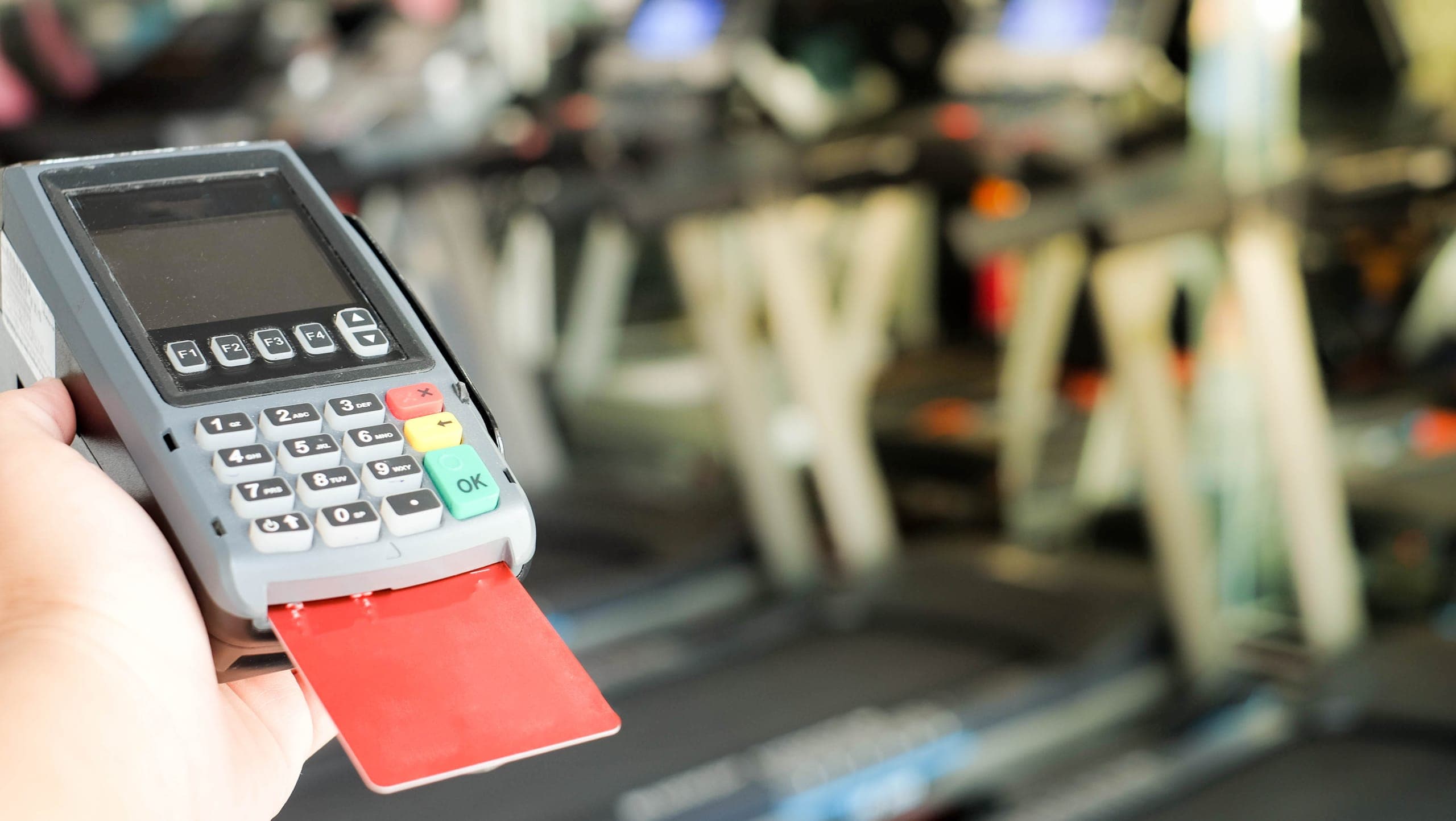 Card reader payment terminal connected to a gym merchant account, with treadmills in the background