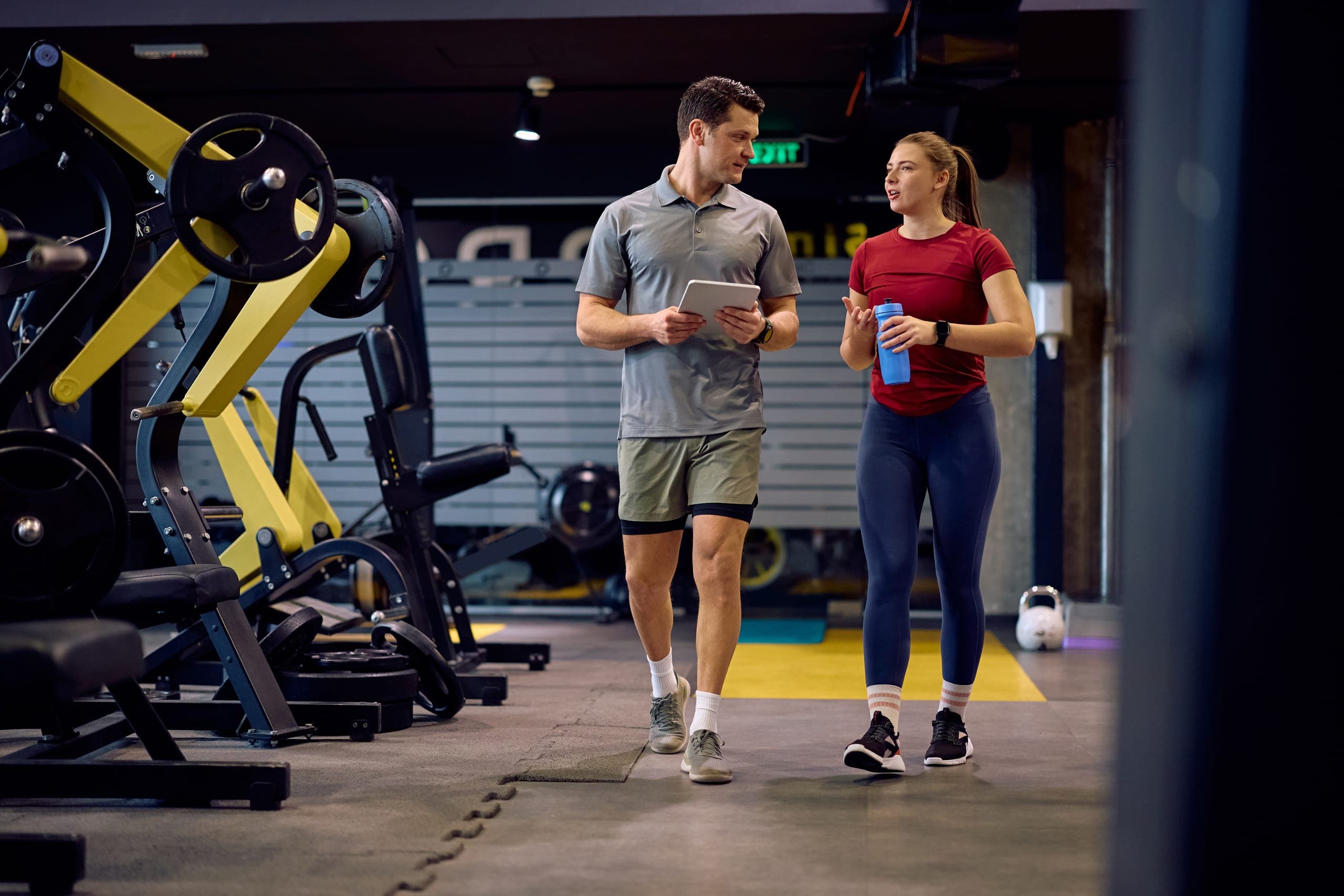 Personal trainer and gym member discussing membership billing while walking through a fitness facility